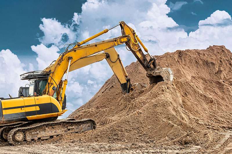 Two excavators dig a large pile of fill dirt at construction site